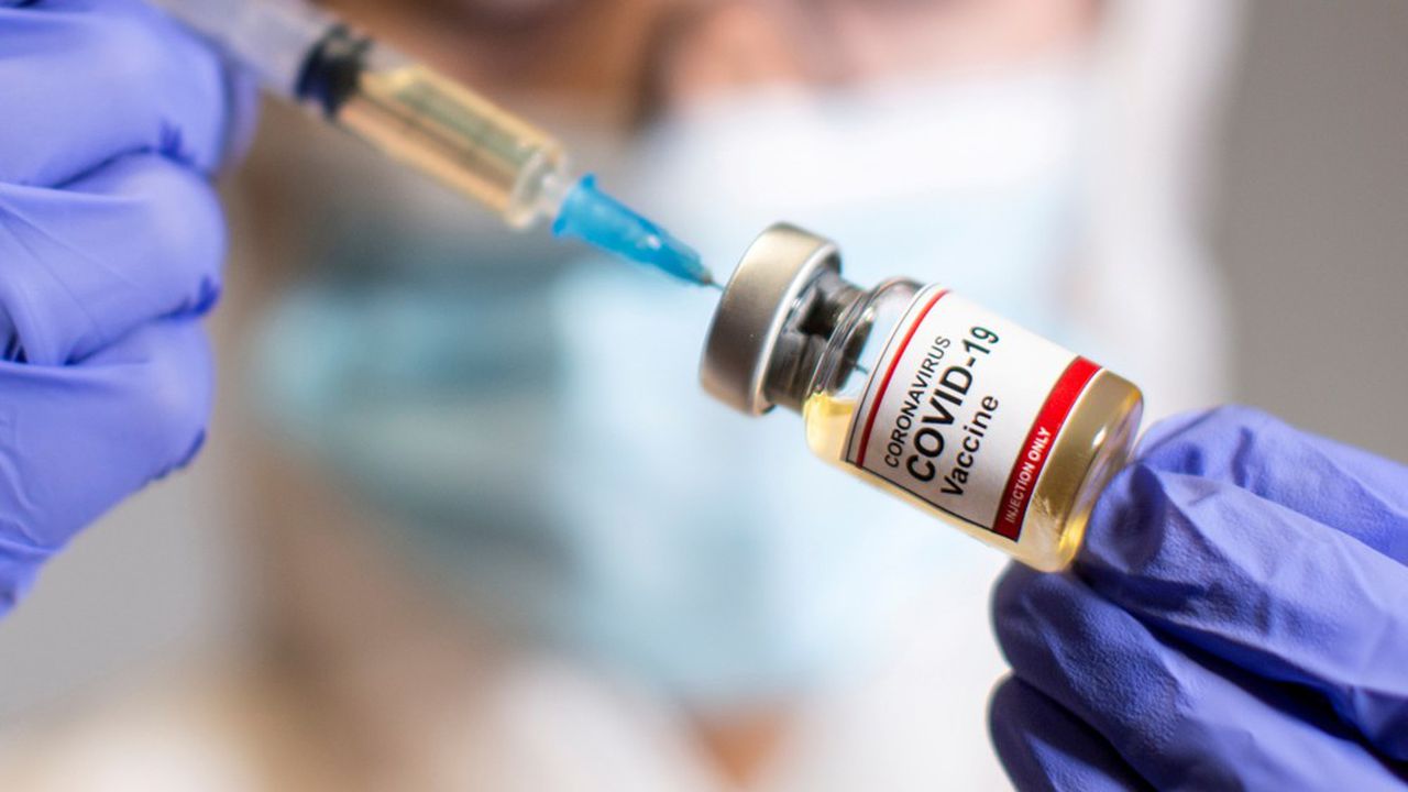 Une femme tient une petite bouteille étiquetée avec un autocollant «Coronavirus COVID-19 Vaccine» et une seringue médicale.