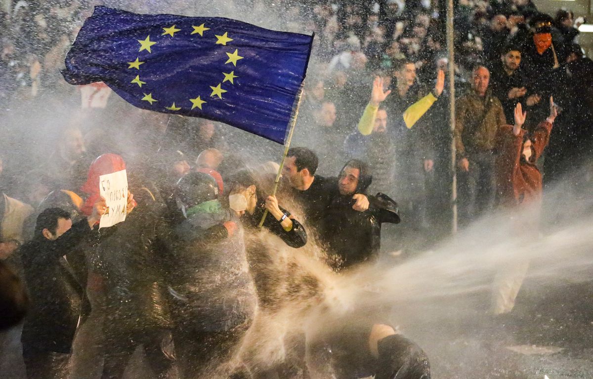 Des manifestants brandissant un drapeau de l'Union européenne alors qu'ils sont aspergés par un canon à eau lors d'affrontements avec la police anti-émeute près du parlement géorgien, à Tbilissi, le 7 mars 2023.