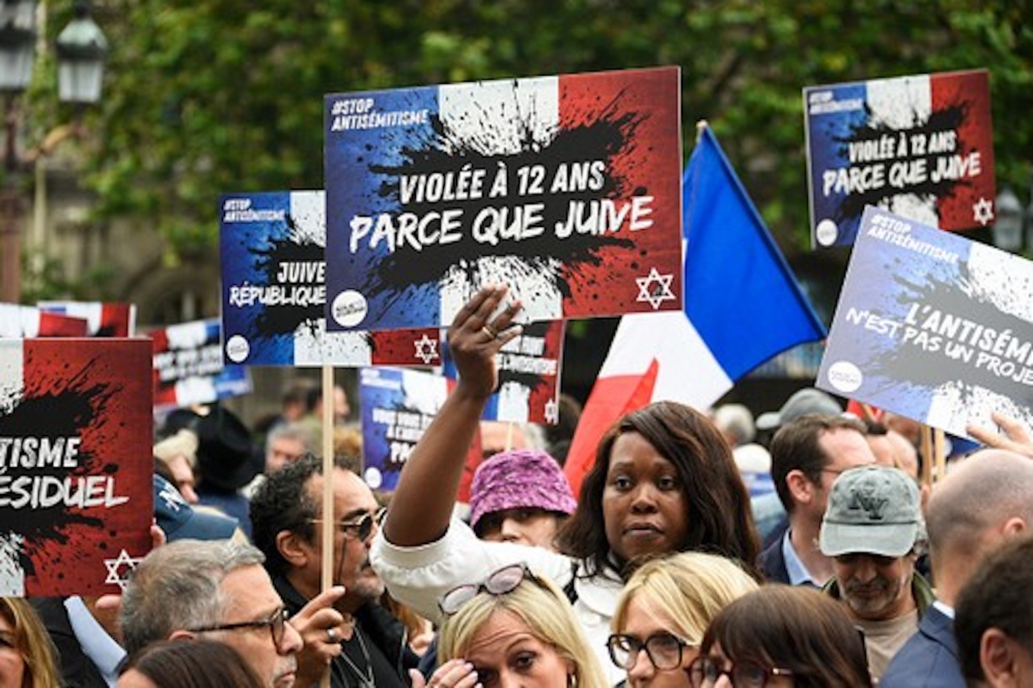 Des manifestants tiennent des pancartes sur lesquelles on peut lire "Violée parce que juive" lors d'un rassemblement pour condamner le viol collectif antisémite d'une jeune fille de 12 ans à Courbevoie, lors d'un rassemblement à Paris le 19 juin 2024, suite à la mise en examen d'adolescents pour viol, menaces de mort, insultes antisémites et violences à son encontre.
