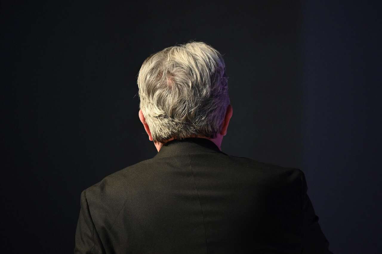 Photo en couleur de Jean-Luc Mélenchon de dos, devant un fond noir.