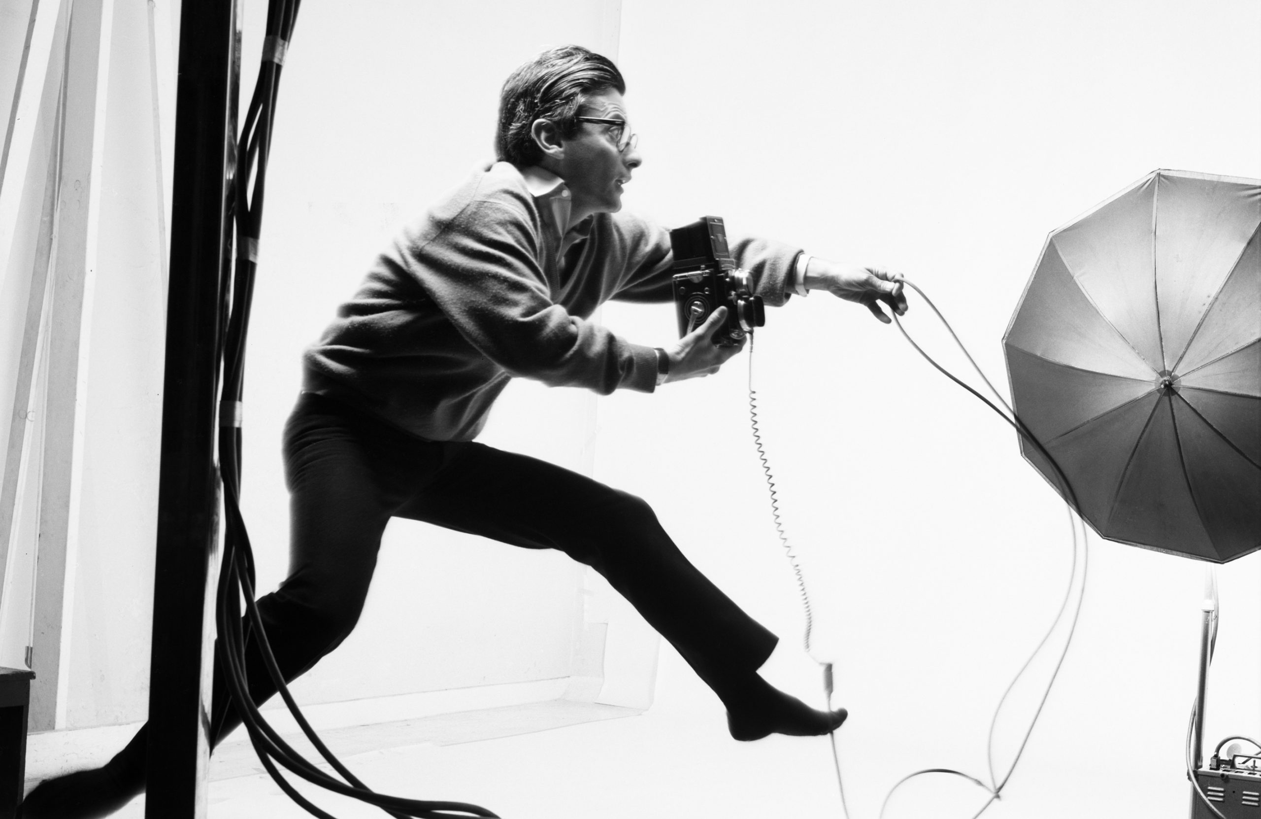 Photo en noir et blanc de Richard Avedon de profil, en train de prendre une photo en sautant dans un studio.