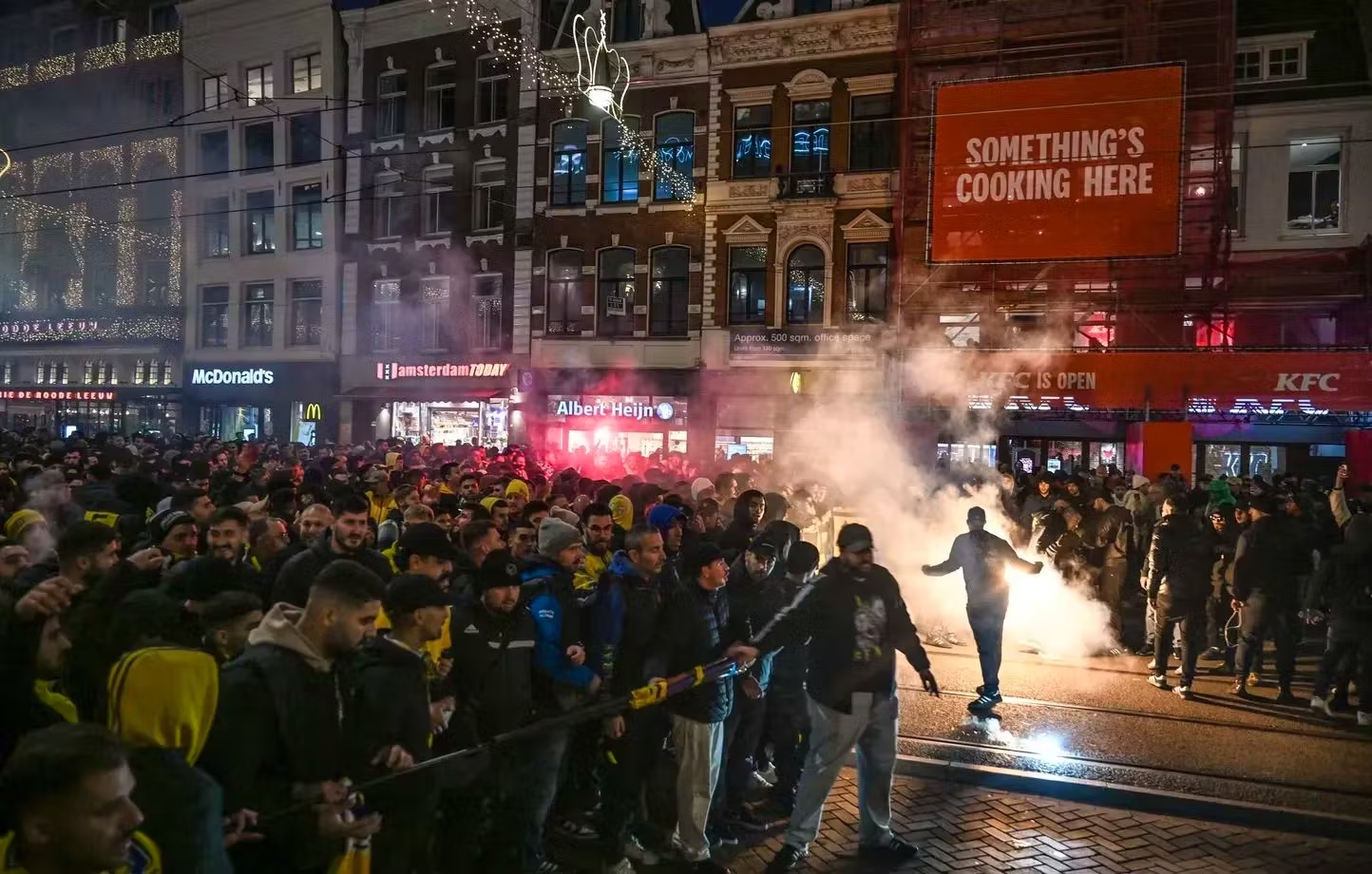 Des supporters de football israéliens sont encadrés par la police, la nuit, dans une rue d'Amsterdam, il y a des fumigènes.