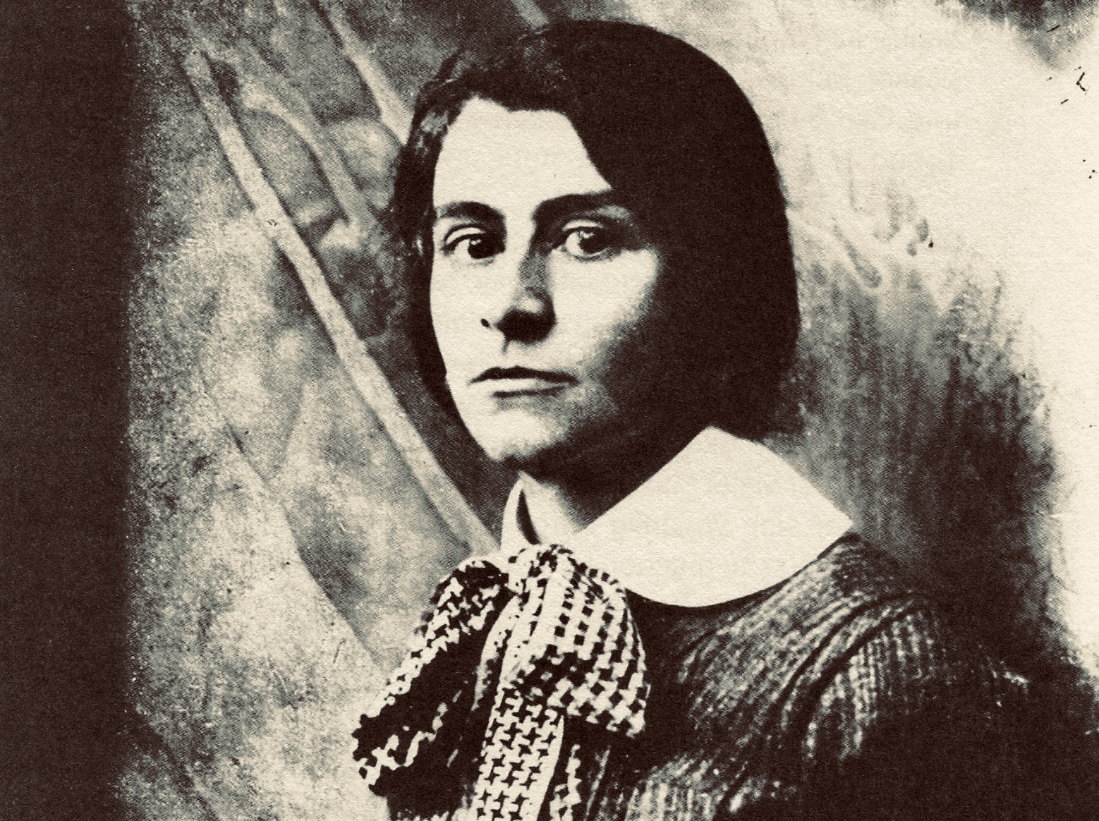 Portrait d'Else Lasker-Schüler, elle a les cheveux mi-longs, regarde l'objectif. Elle porte une tenue avec un grand col claudine blanc et une noeud a carreaux au niveau de ce col.