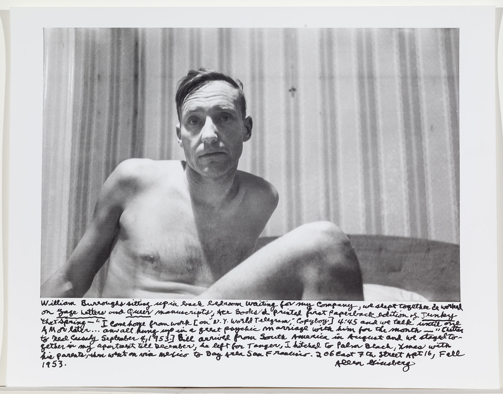 Portrait en noir et blanc de William S. Burroughs, qui semble nu, assis dans un lit. On voit son torse et l'une de ses jambes. Sous la photo on peut lire un texte manuscrit de 8 lignes signé par Allen Ginsberg.