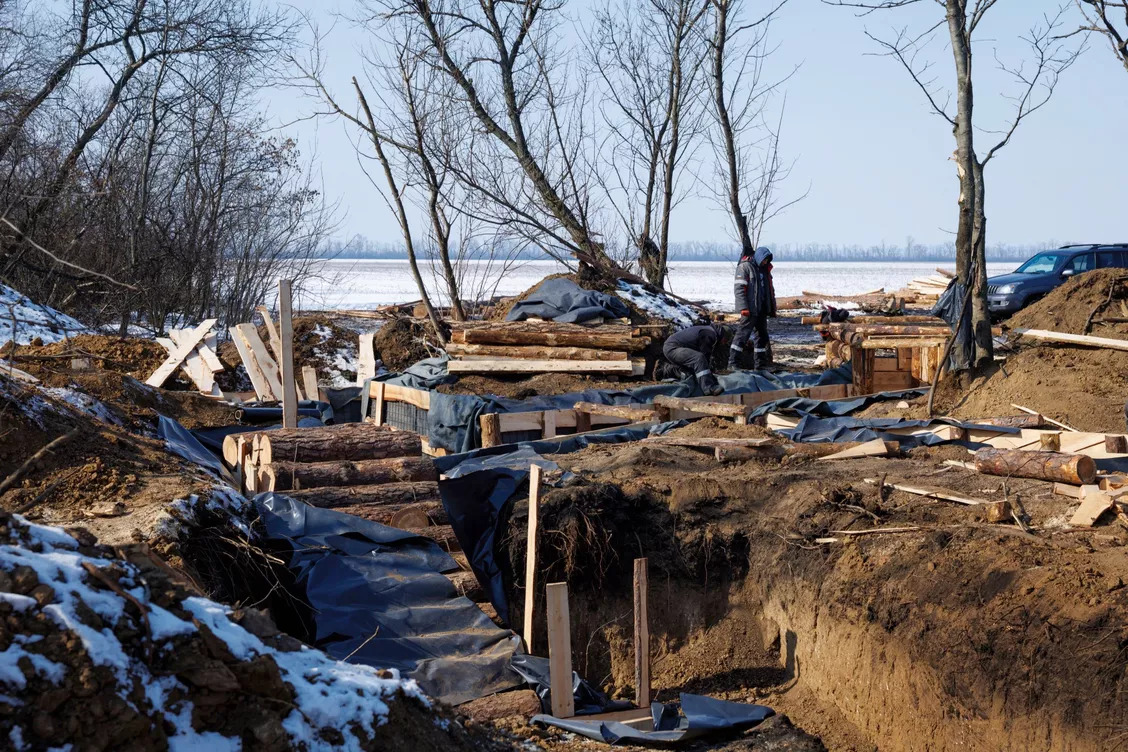 En marge d'une pleine enneigée deux hommes fortifient des tranchées pour construire un abri souterrain. On voit de grands trois et de grandes tranchées et des buches et morceaux de bois recouvrir le sol terreux.