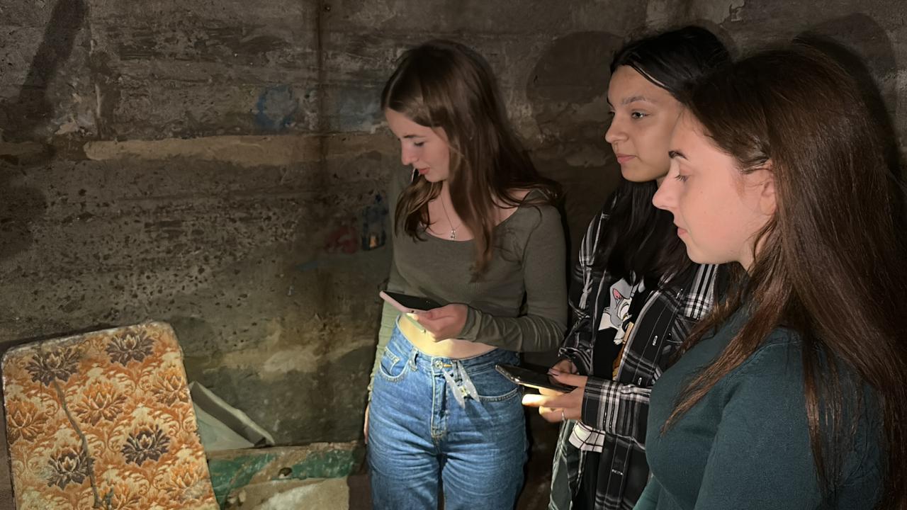 Maryna, Daryna et Anastasia, trois adolescentes, éclairent une cave avec les flashs de leurs téléphones.