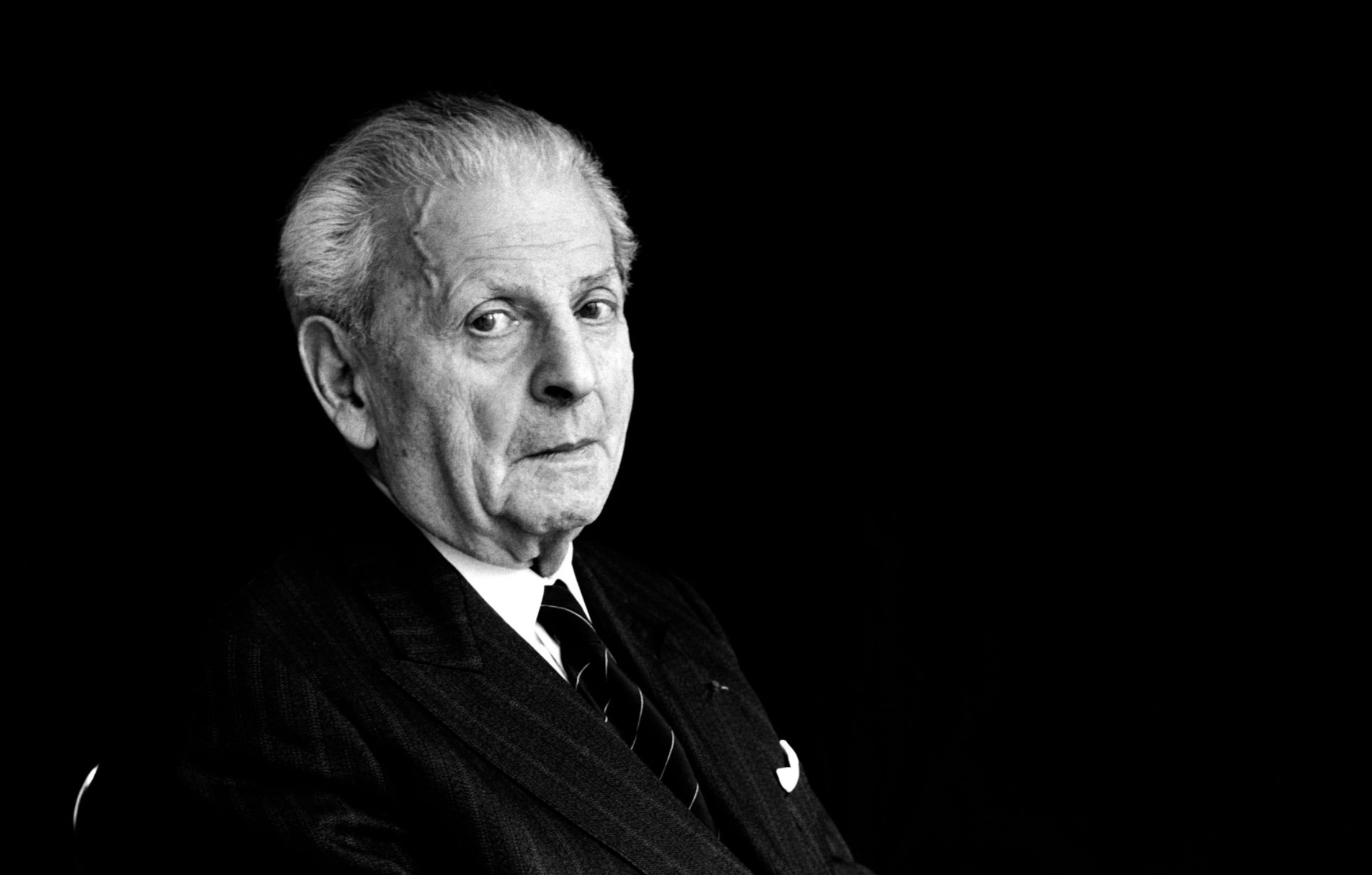 Portrait en noir et blanc d'Emmanuel Levinas, en costume. Il est assis devant un font noir et regarde l'objectif.