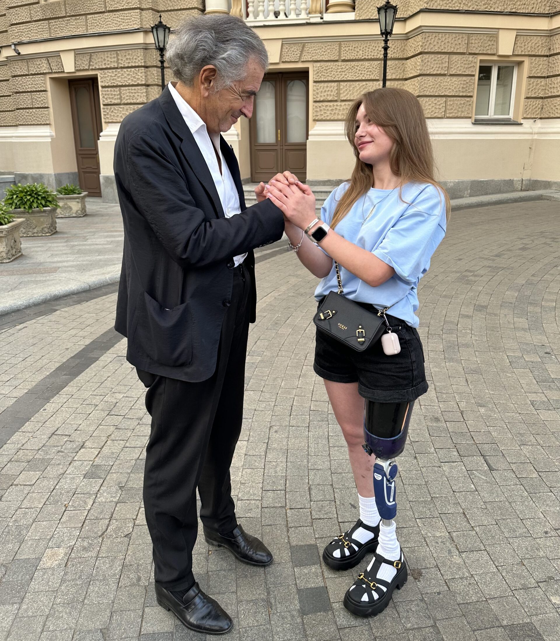 Bernard-Henri Lévy tient les mains d'une jeune ukrainienne dont une jambe a été amputée, elle porte une prothèse.