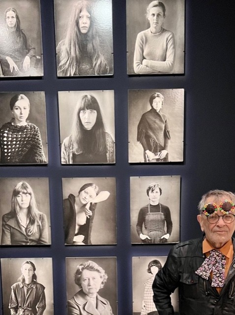 Fernando Arrabal pose a coté de portraits de femmes en noir et blanc.
