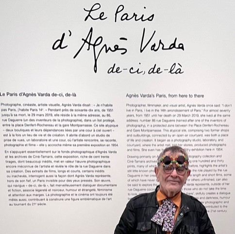 Fernando Arrabal visite l’exposition « Le Paris d’Agnès Varda », au Musée Carnavalet. Il pose devant un carton explicatif de l'exposition.
