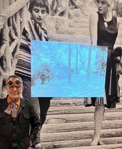 Fernando Arrabal visite l’exposition « Le Paris d’Agnès Varda », au Musée Carnavalet. Il pose devant une grande photo d'Agnès Varda jeune.