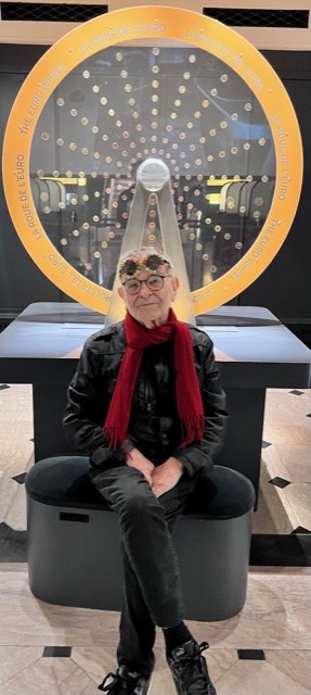 Fernando Arrabal à la Cité de l'Economie, le dramaturge espagnol est assis devant une roue de l'euro, roue en métal et en verre composée de pièces de monnaie.