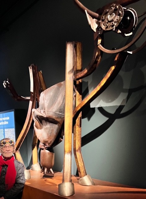 A la Cité de l'Economie Fernando Arrabal pose devant une sculpture en métal représentant de manière abstraite une vache.
