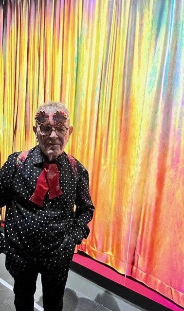 Fernando Arrabal visite l’exposition « Les Sept Sens Célestes » à l’Hôtel de la Marine. Il pose devant une oeuvres abstraite multicolore.