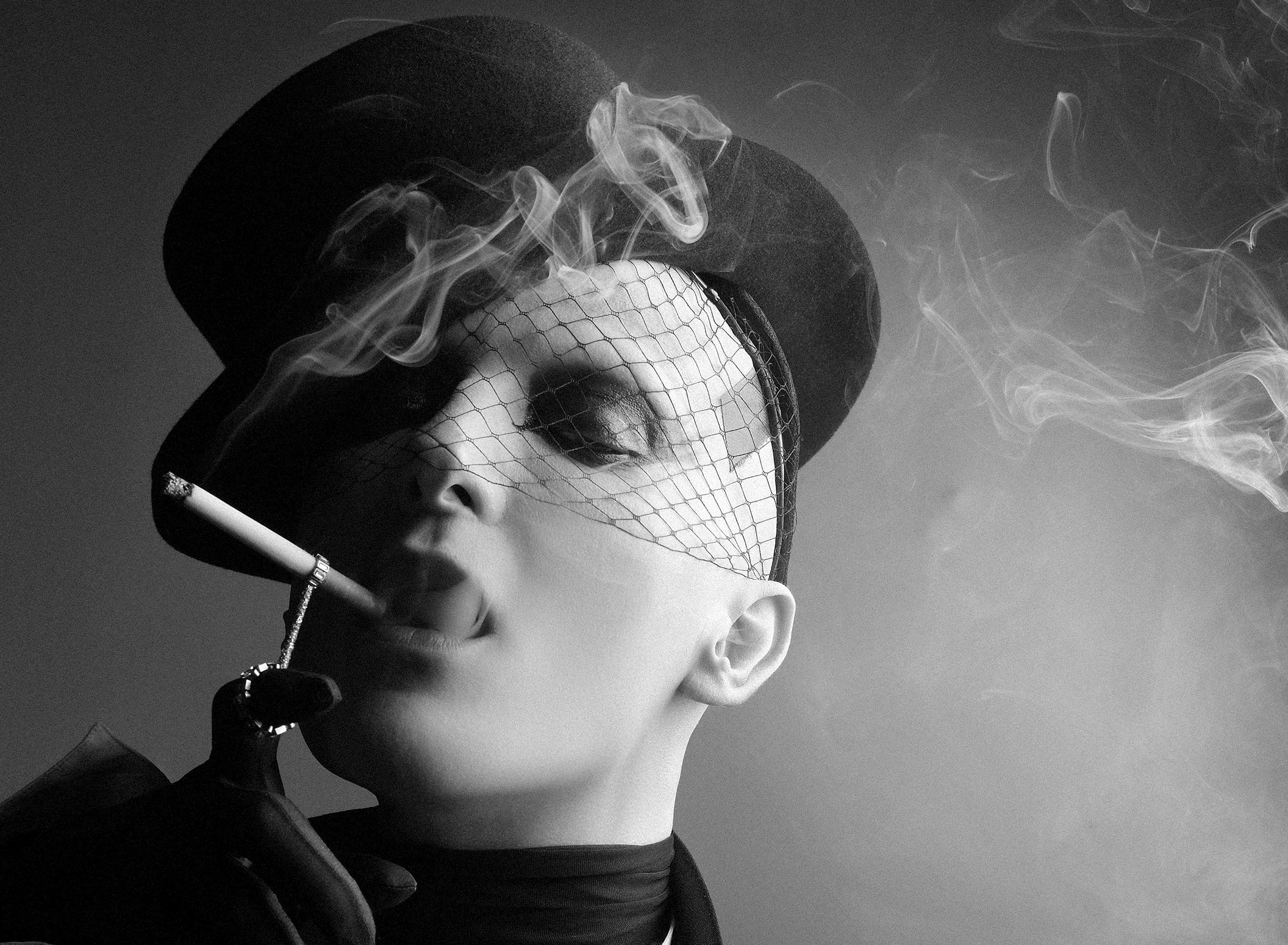 Portrait en noir et blanc du photographe ali mahdavi avec un chabeau haut de forme noir, il fume une cigarette accrochée à une bague.