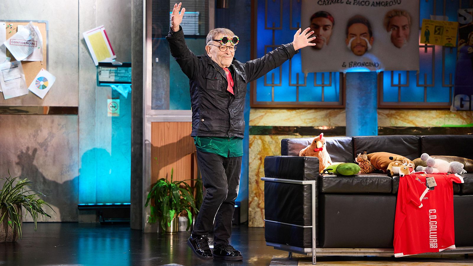 Le poète et dramaturge Fernando Arrabal sur le plateau de l'émission emblématique de la télévision espagnole, La Revuelta, animée par David Broncano. Le décor, un appartement aux couleurs vives, sert de toile de fond tandis qu'Arrabal se tient debout, les bras écartés.