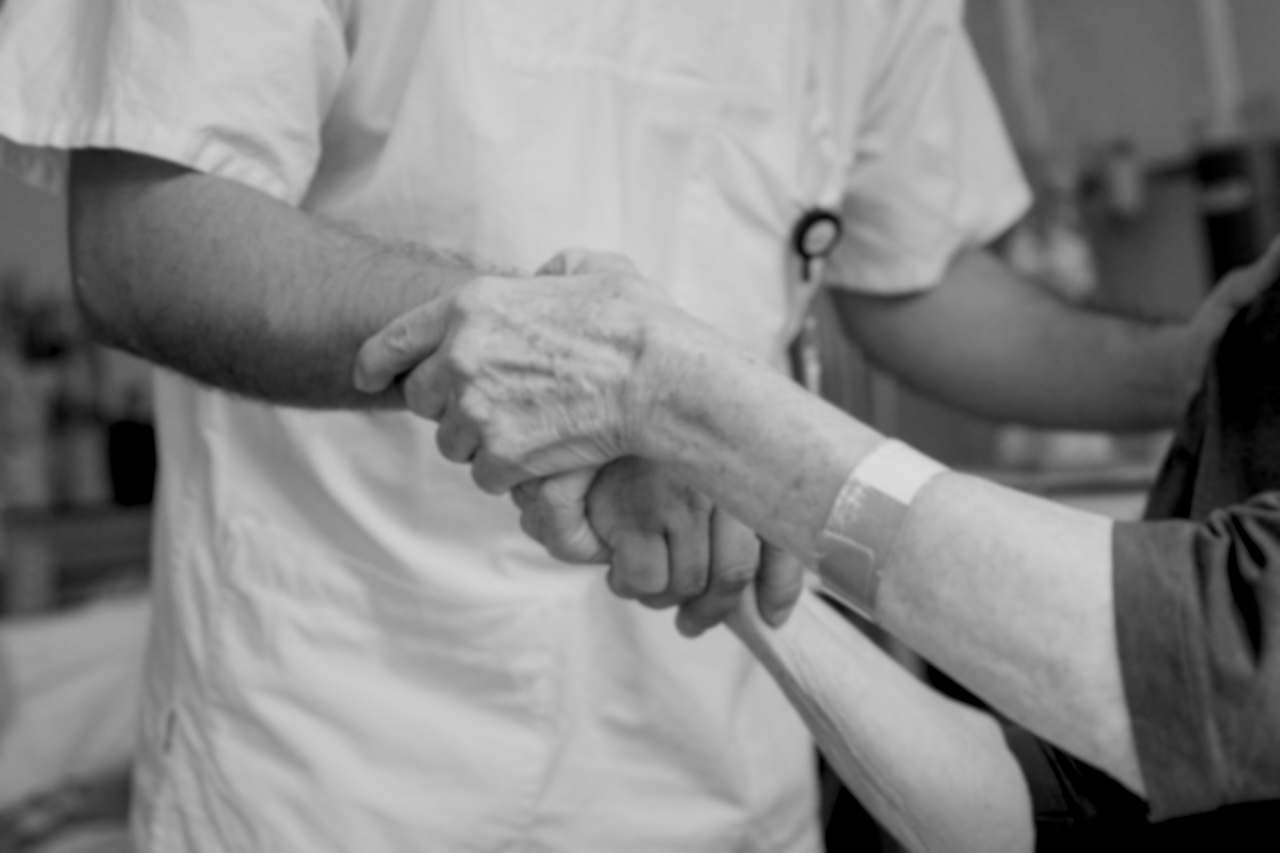 Photographie montrant les mains d’un patient hospitalisé serrant la main d’un médecin vêtu d’une blouse blanche.