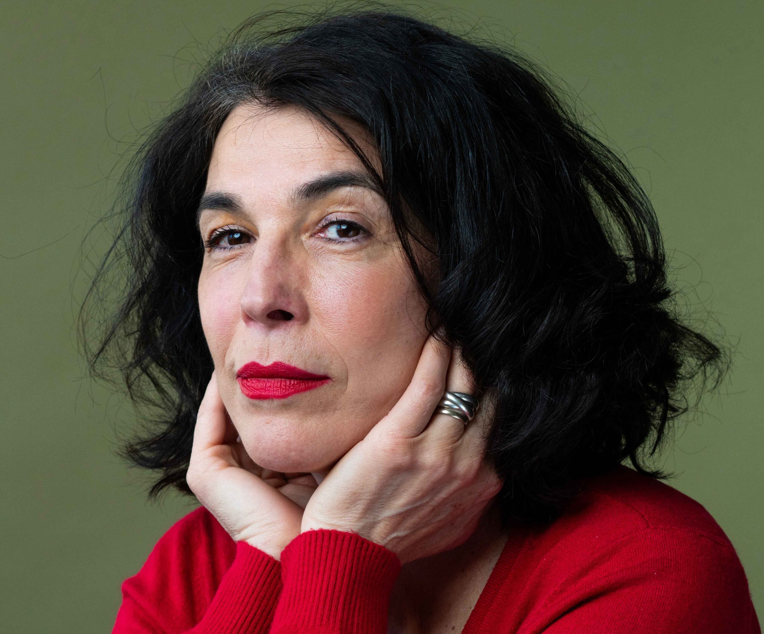 Portrait en couleurs de Cécile Guilbert, elle porte un pull rouge et a le visage posé dans ses mains.