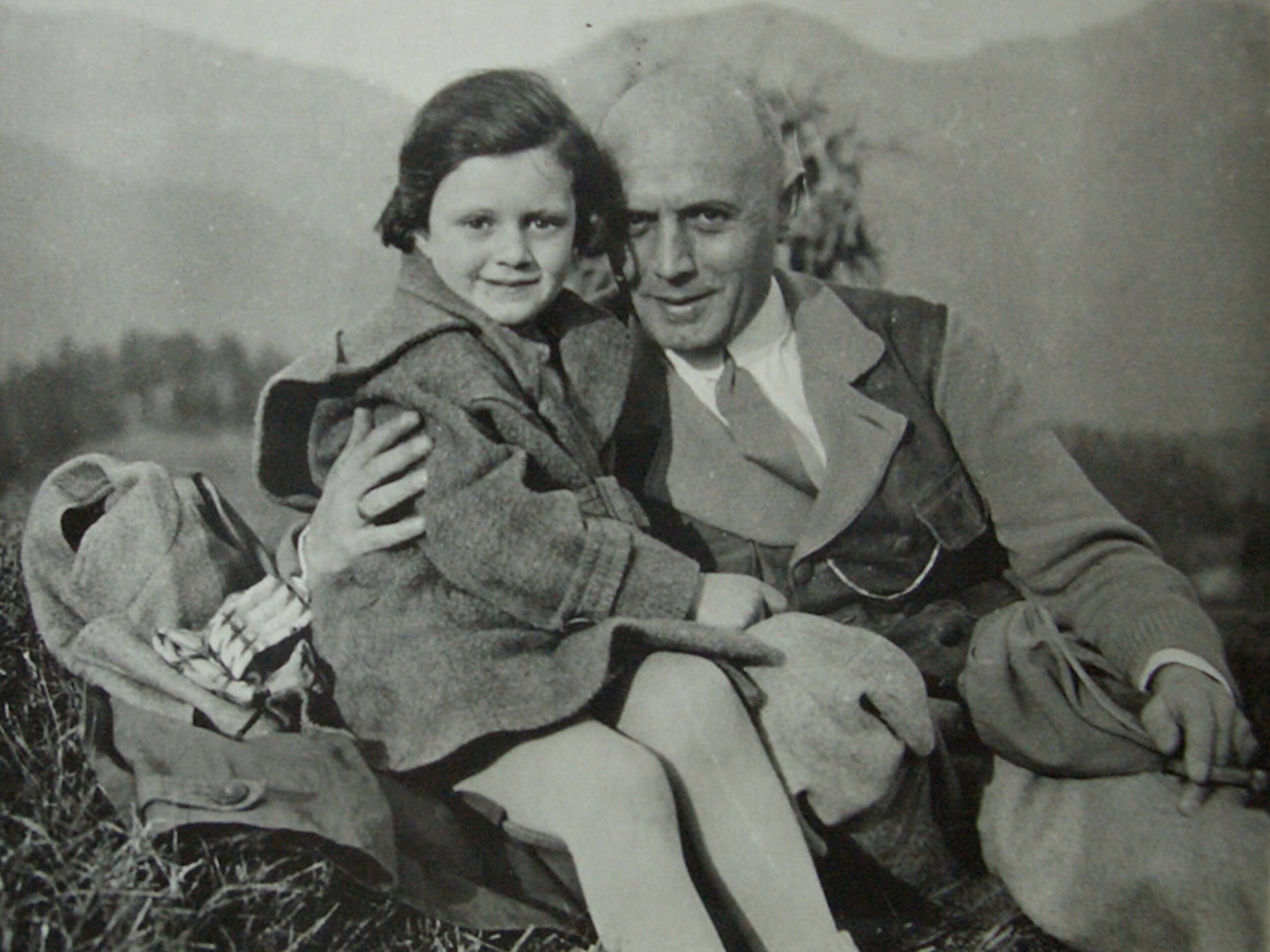 Photo en noir et blanc de la petite fille Ilse Brüll et son père, Rudolf. Ils sont assis dans l'herbe à la montagne.