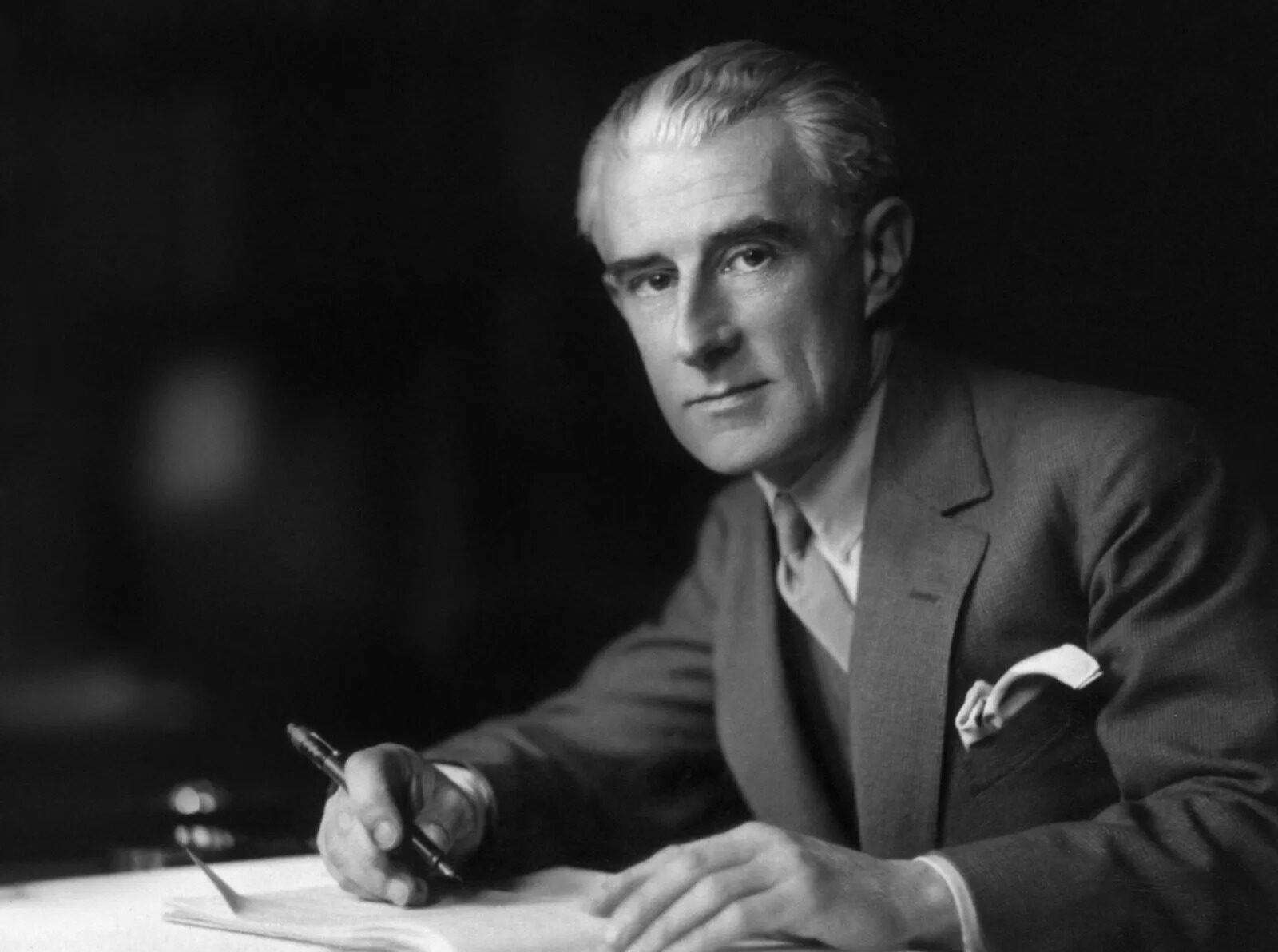 Photo en noir et blanc du compositeur français Maurice Ravel, assis, en train d'écrire.