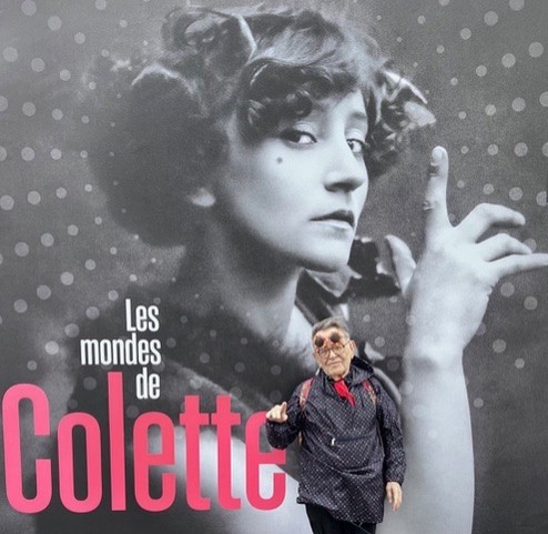 Fernando Arrabal a visité l’exposition « Les mondes de Colette » à la BNF (Bibliothèque Nationale de France). Il pose devant un grand portrait de Colette en noir et blanc.