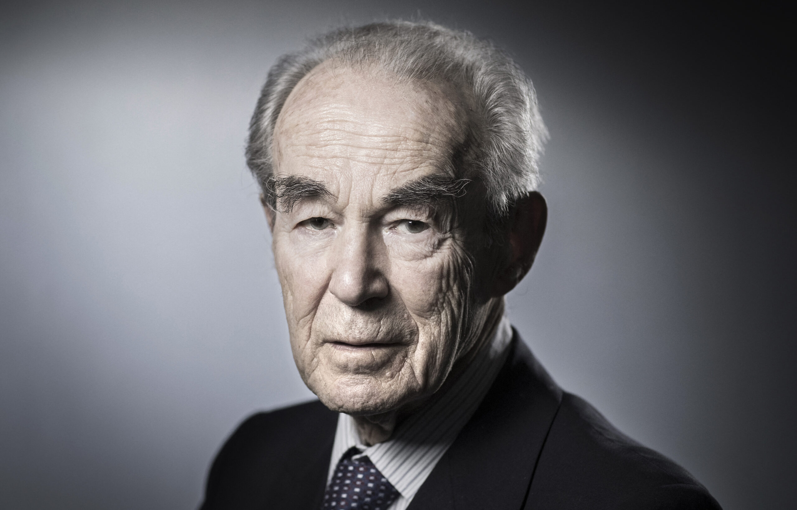 Portrait de Robert Badinter devant un fond gris.