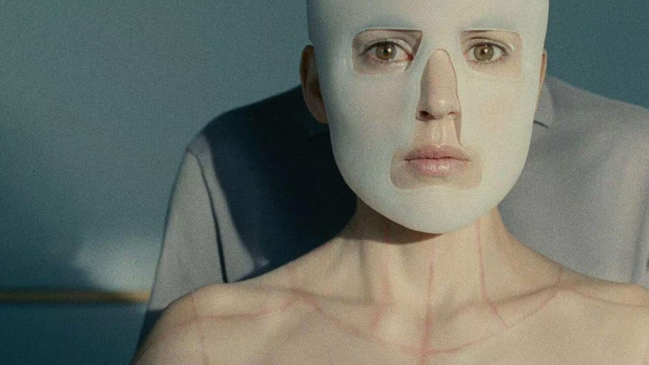 Elena Anaya dans « La piel que habito » de Pedro Almodovar (2011). Elle porte un masque, on voit des cicatrices sur son cou ; on distingue un homme derrière elle.