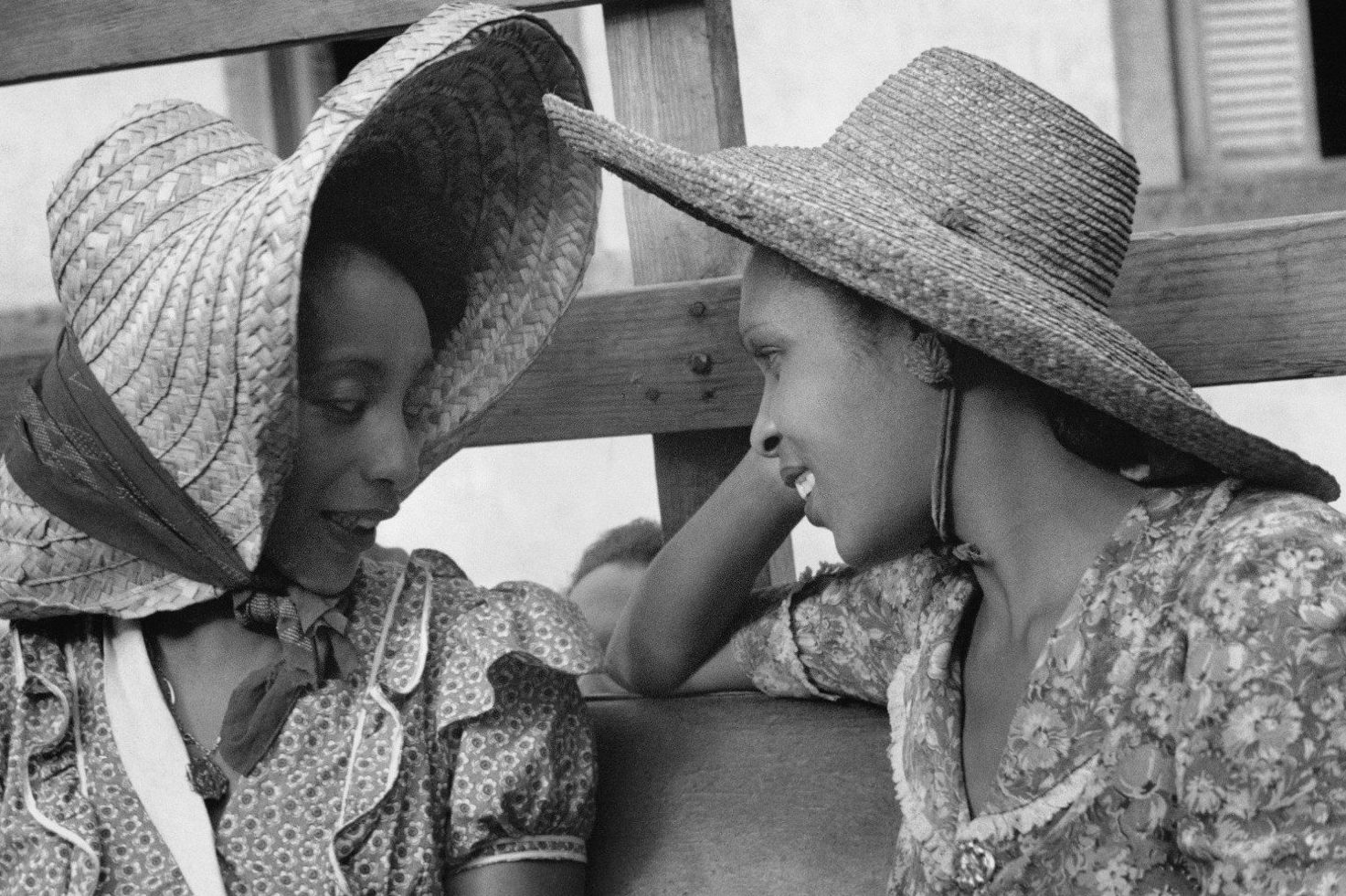 Photo en noir et blanc de Mireille Maugée et Suzanne Césaire en train de ses parler, elles portent des robes à fleurs et des chapeaux à larges bords.