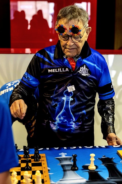 Fernando Arrabal lors d’un tournois d’échecs, il est debout devant un jeu d'échecs il porte le maillot de l'équipe d'échecs de Melilla.