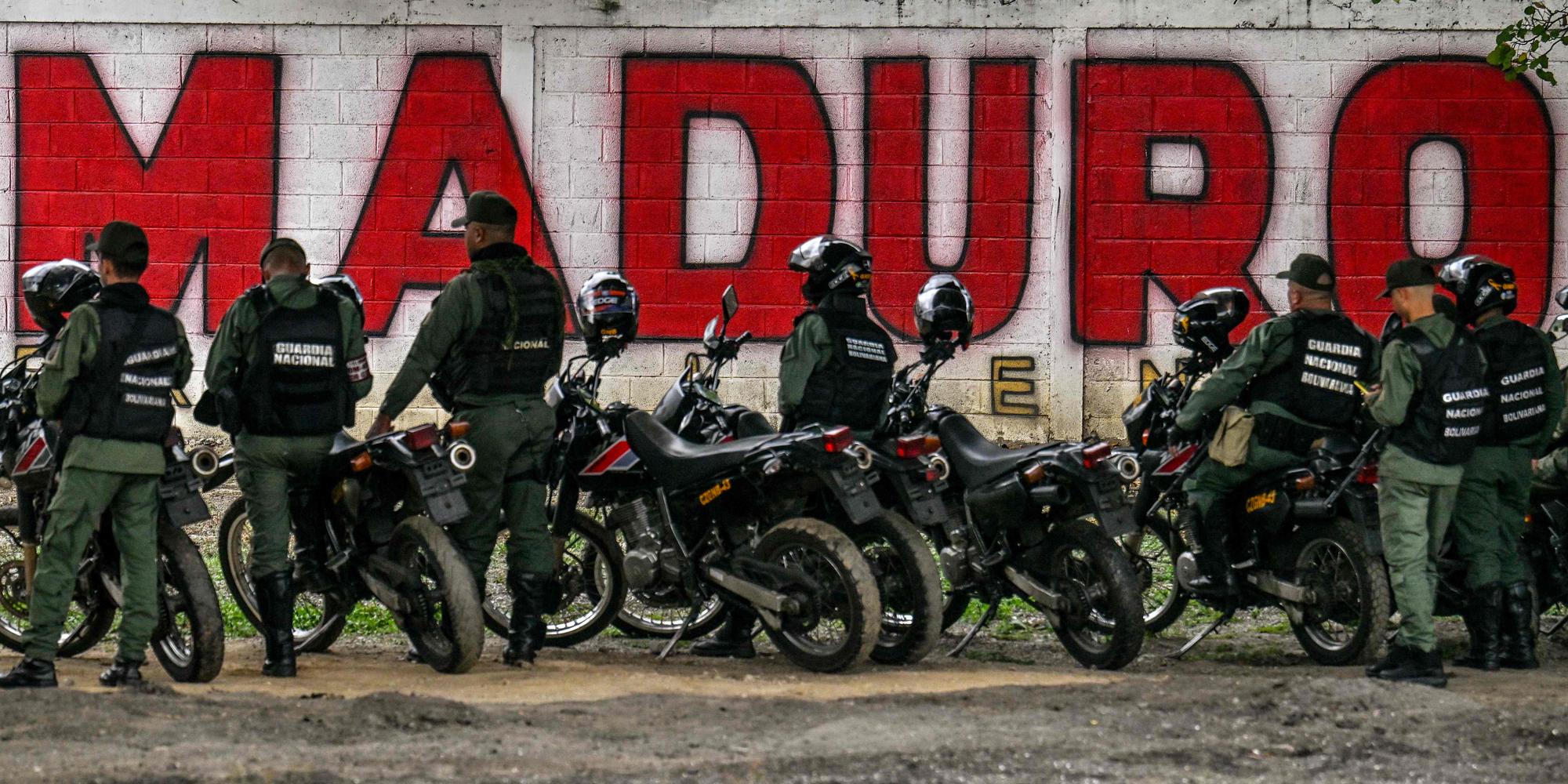 Devant un mur où figure un tag avec le nom de Nicolas Maduro, se tiennent des membres de la garde nationale vénézuélienne, à Caracas.