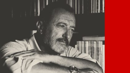 La grand écrivain espagnol Arturo Pérez-Reverte pose les bras croisés, assis, devant sa bibliothèque.