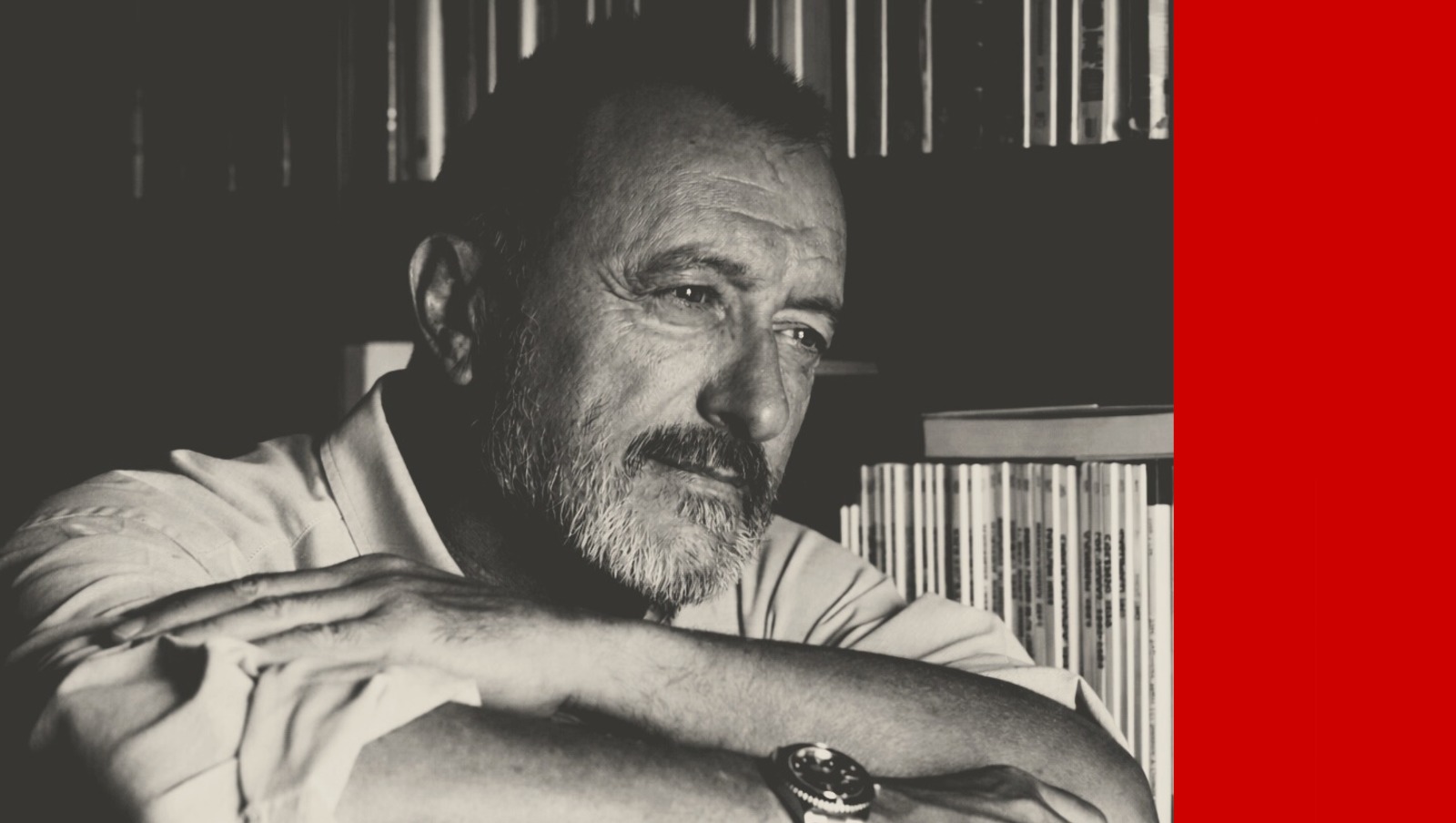 La grand écrivain espagnol Arturo Pérez-Reverte pose les bras croisés, assis, devant sa bibliothèque.