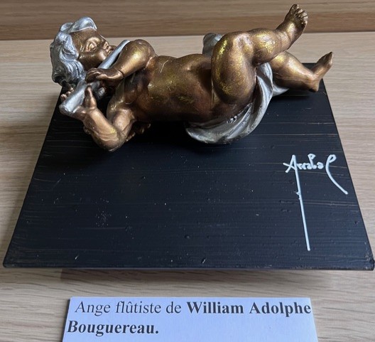 Poème plastique de Fernando Arrabal. On voit un petit ange jouer de la flûte, la sculpture est posée sur un petit socle noir.