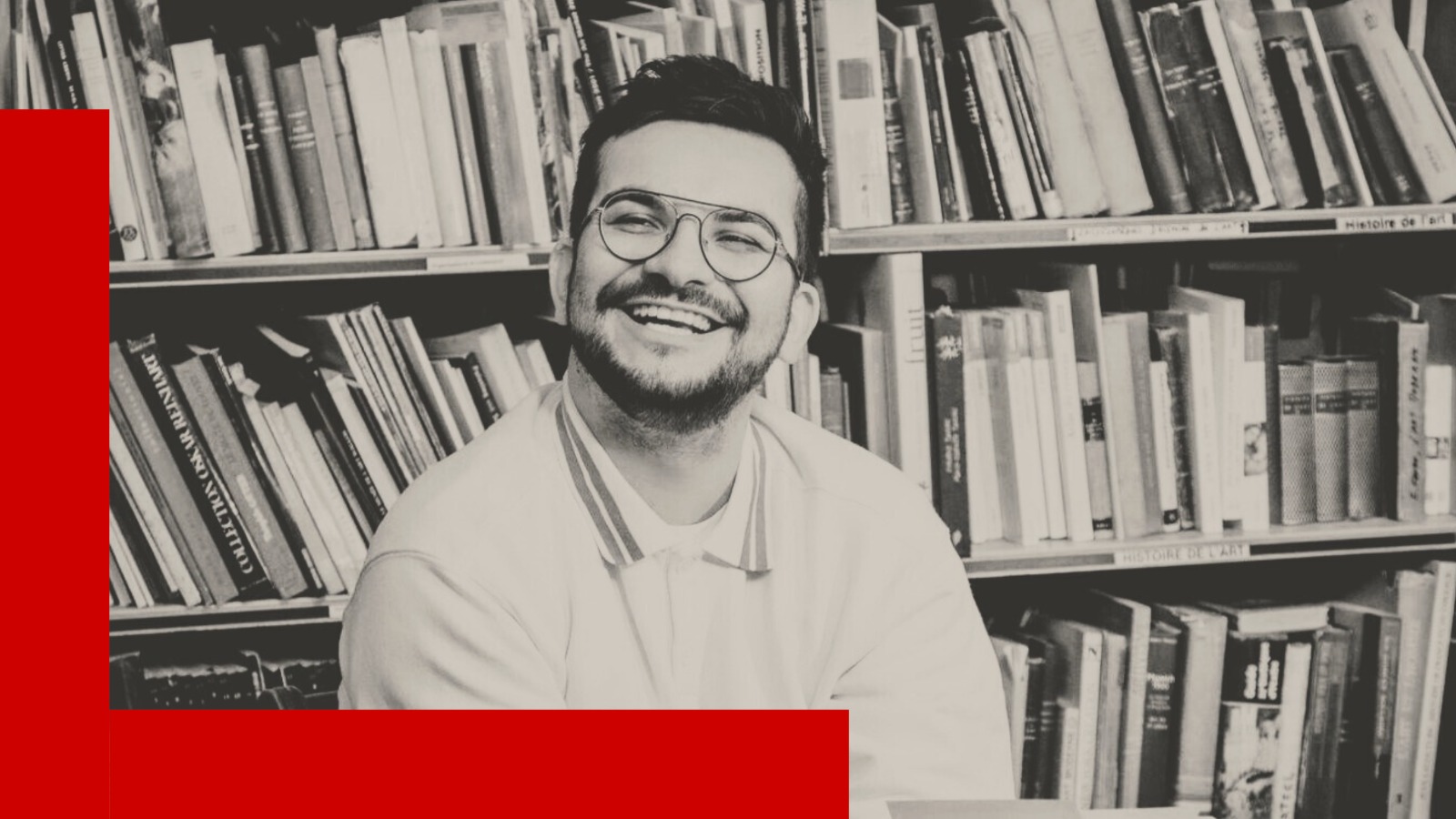 L'influenceur littéraire François Coune assis devant les étagères d'une bibliothèque remplie de livres.