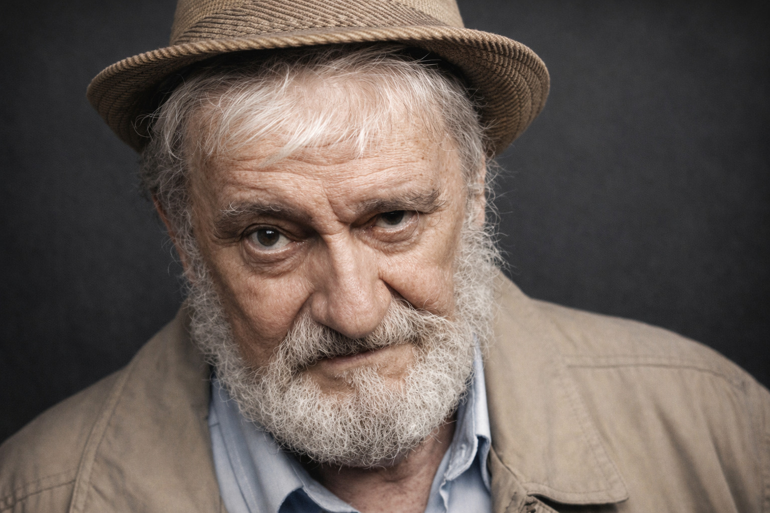 Portrait en couleurs de Georges-Olivier Châteaureynaud, il porte un chapeau et pose devant un fond unis gris.