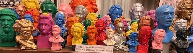 Une vingtaine de statuettes de bustes d'hommes célèbres peints de manière multicolore.
