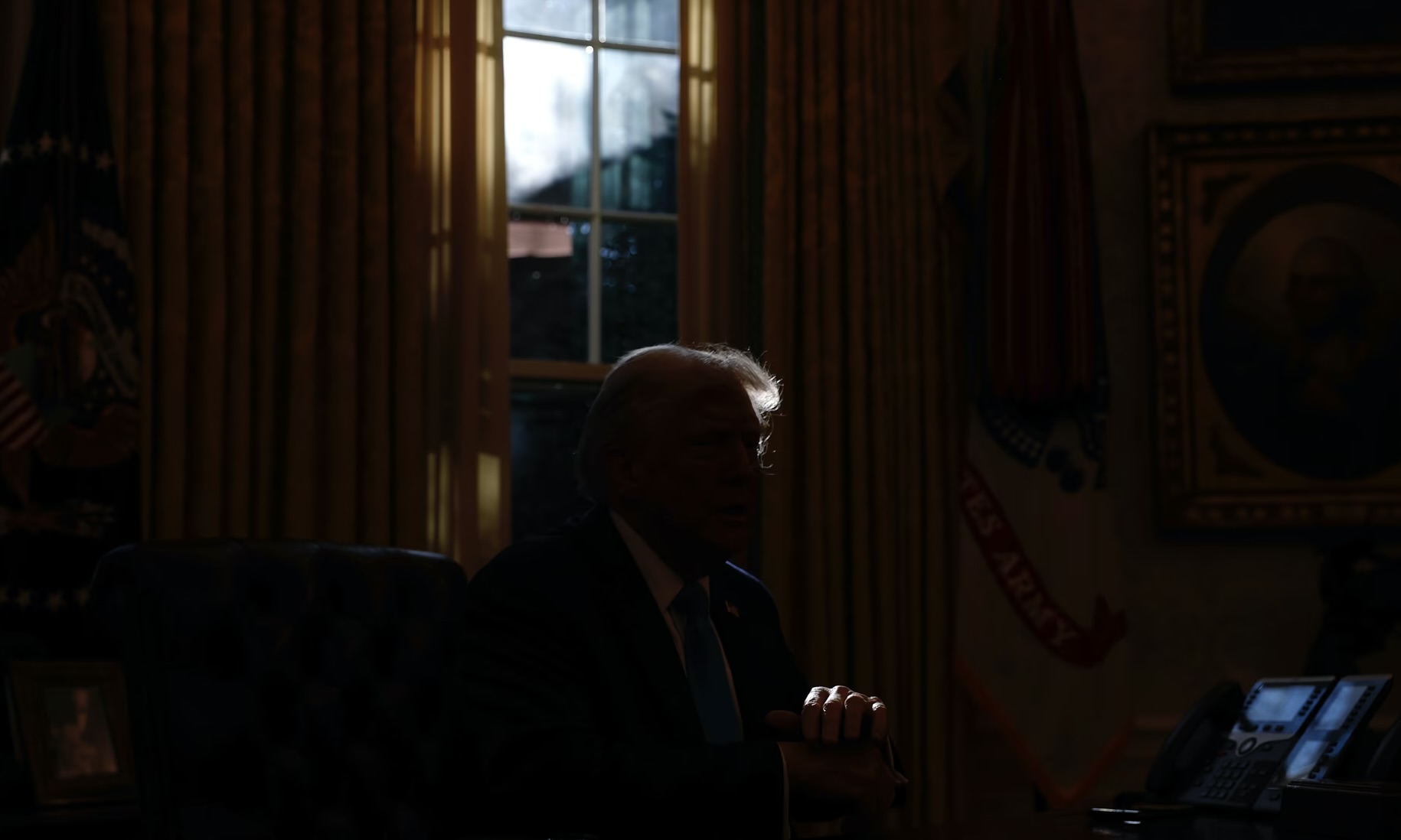 Portrait de Donald Trump dans l'ombre assis à son bureau, on ne distingue sur sa coiffure.