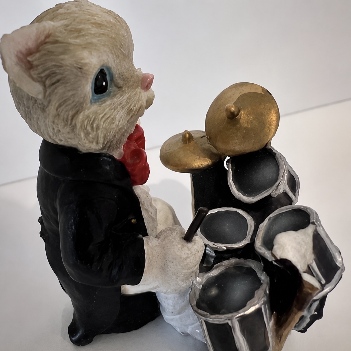 Figurine de chat en costume noir jouant d’une batterie miniature.
