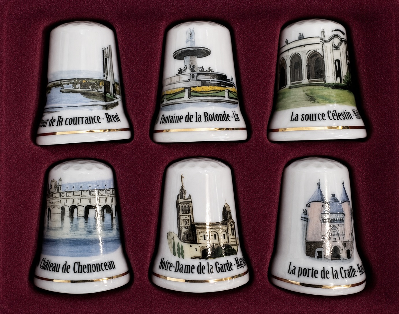 Lot de six dés à coudre en porcelaine décorés de monuments, présentés dans un écrin rouge.