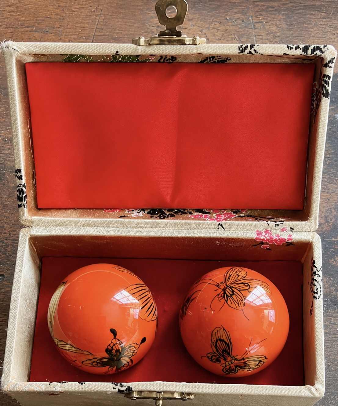 Petit coffret rectangulaire à intérieur rouge contenant deux boules orange décorées de motifs noirs.