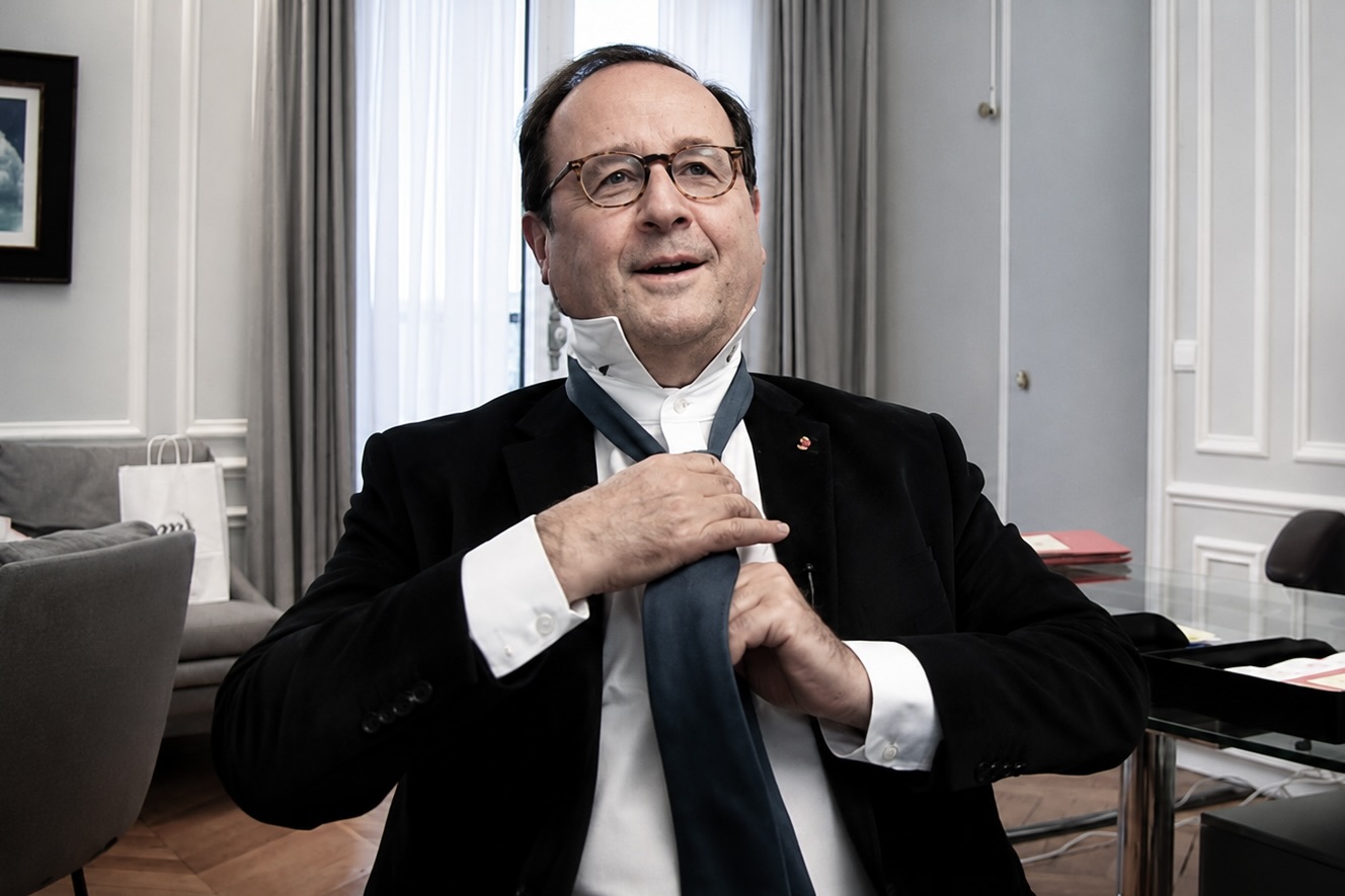 François Hollande est assis, il ajuste sa cravate dans un bureau.