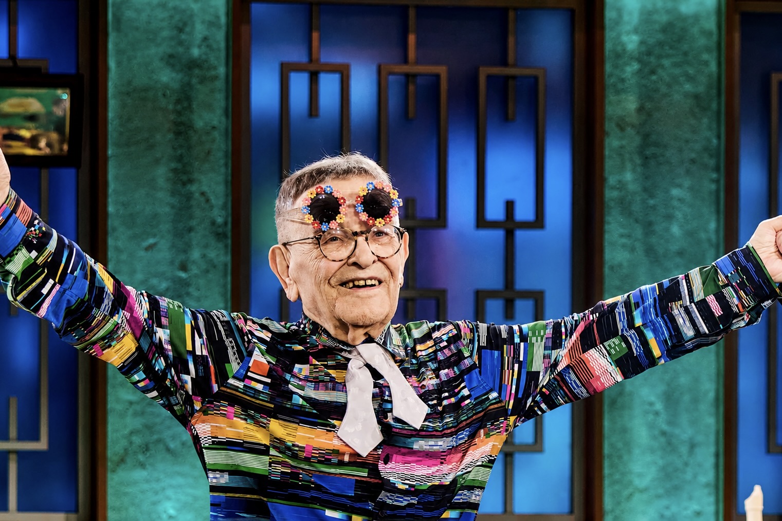 Fernando Arrabal dans une tenue colorée a les bras levés et écartés.