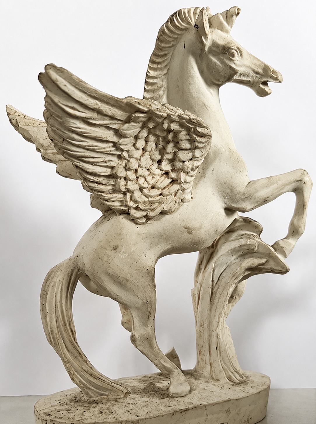 Une statuette en matériau clair représentant un cheval ailé cabré, posé sur un socle sculpté.