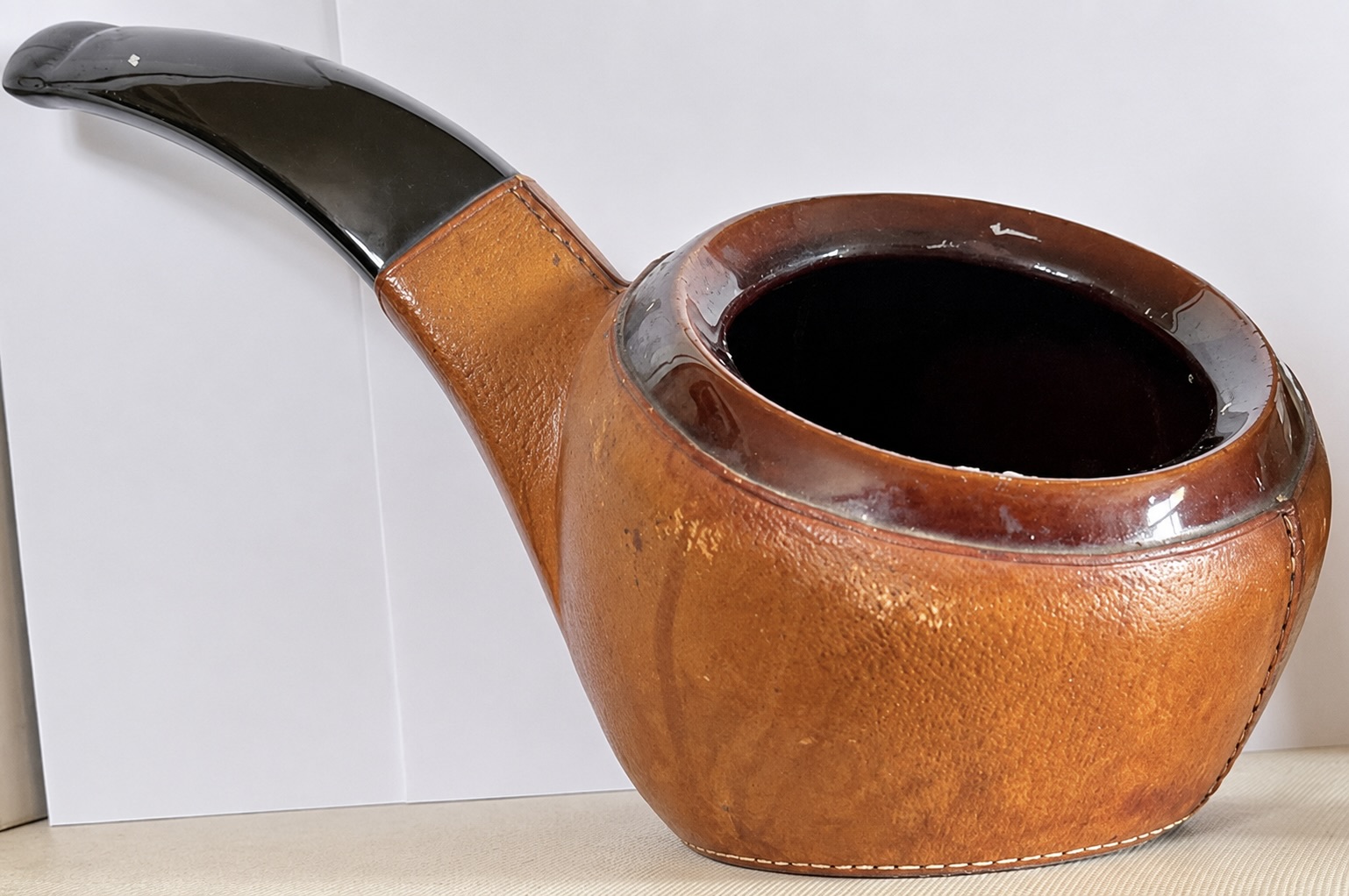 Une pipe en bois brun à embouchure noire est photographiée de profil sur un fond blanc uni.