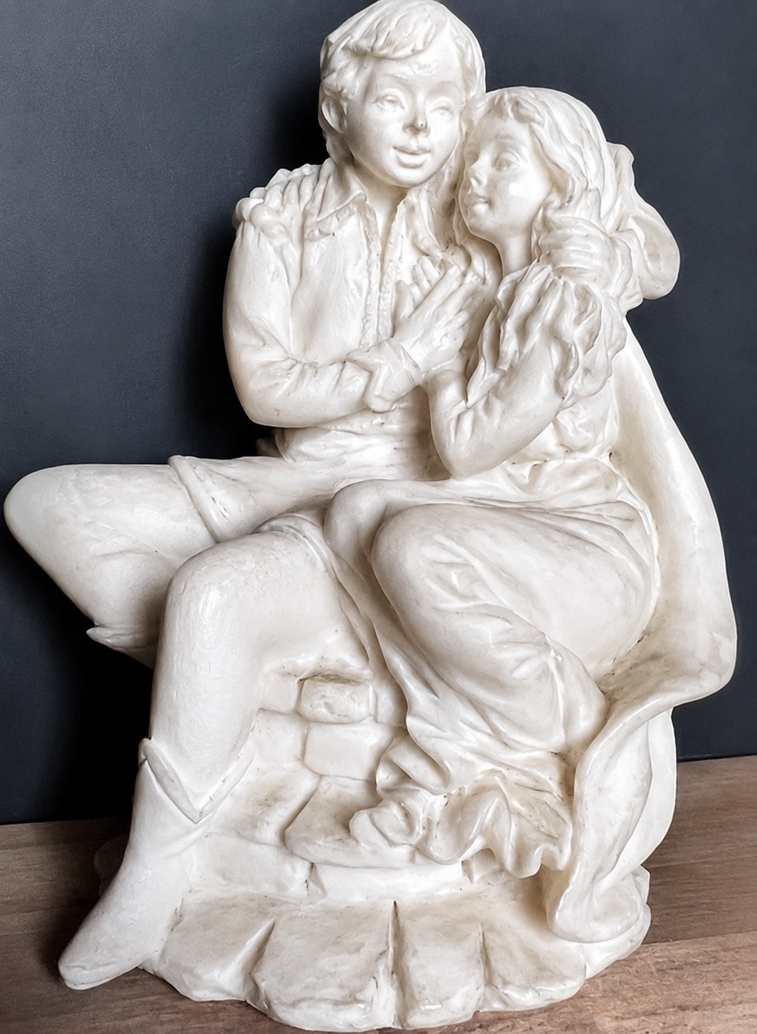 Sculpture blanche représentant deux jeunes personnages assis enlacés sur un socle.