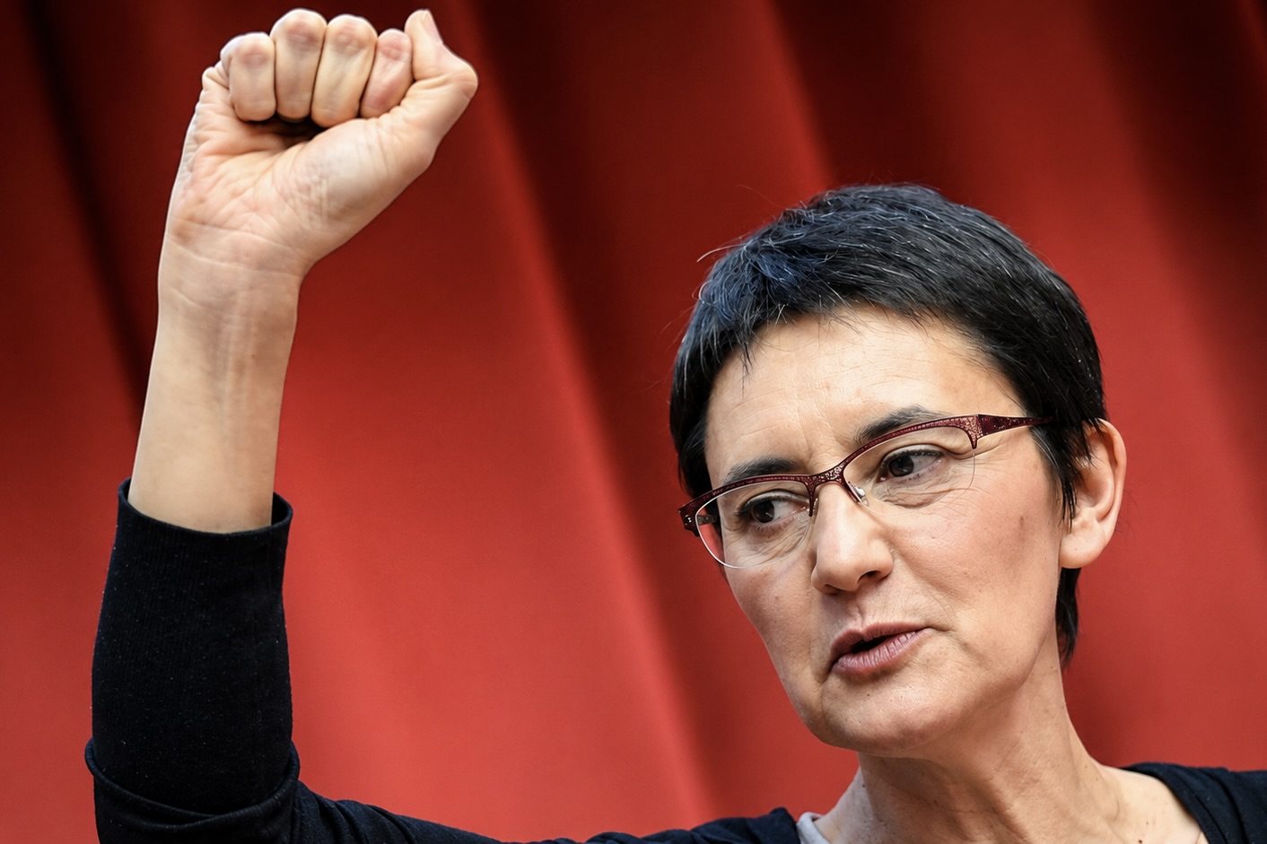 Nathalie Arthaud le poing levé devant un fond rouge.