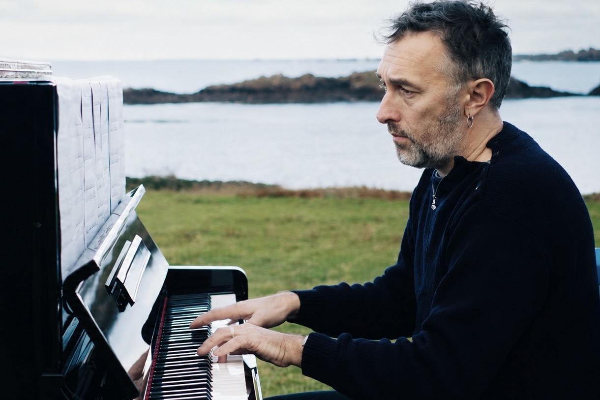 Yann Tiersen joue du piano au bord de la mer.