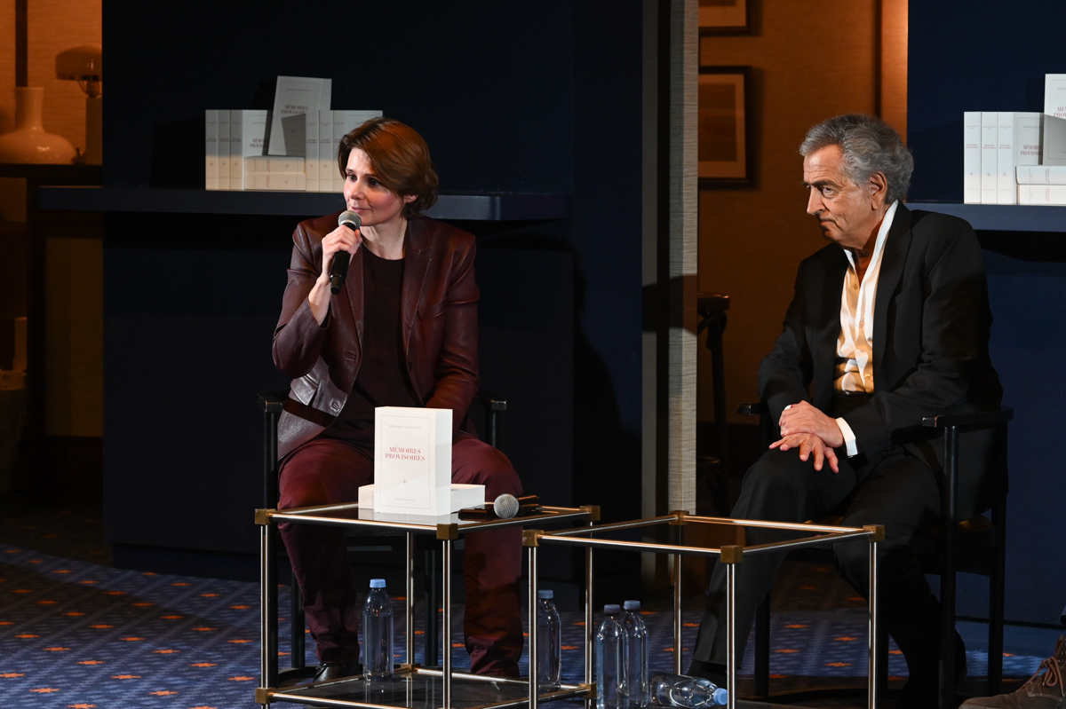 Caroline Fourest lors de la soirée de lancement de « Mémoires provisoires » de Bernard-Henri Lévy ; elle parle dans un micro, BHL est assis près d'elle.