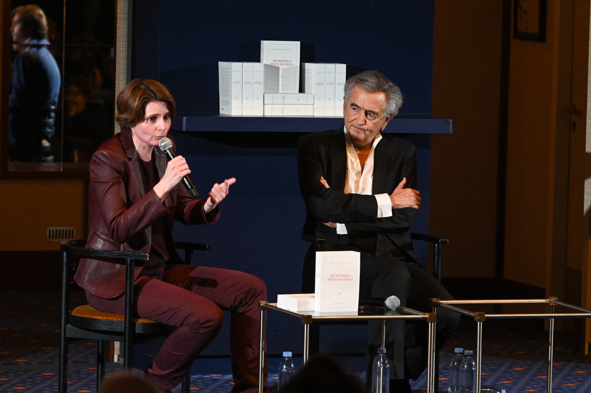 Caroline Fourest lors de la soirée de lancement de « Mémoires provisoires » de Bernard-Henri Lévy ; elle parle dans un micro, BHL est assis près d'elle.