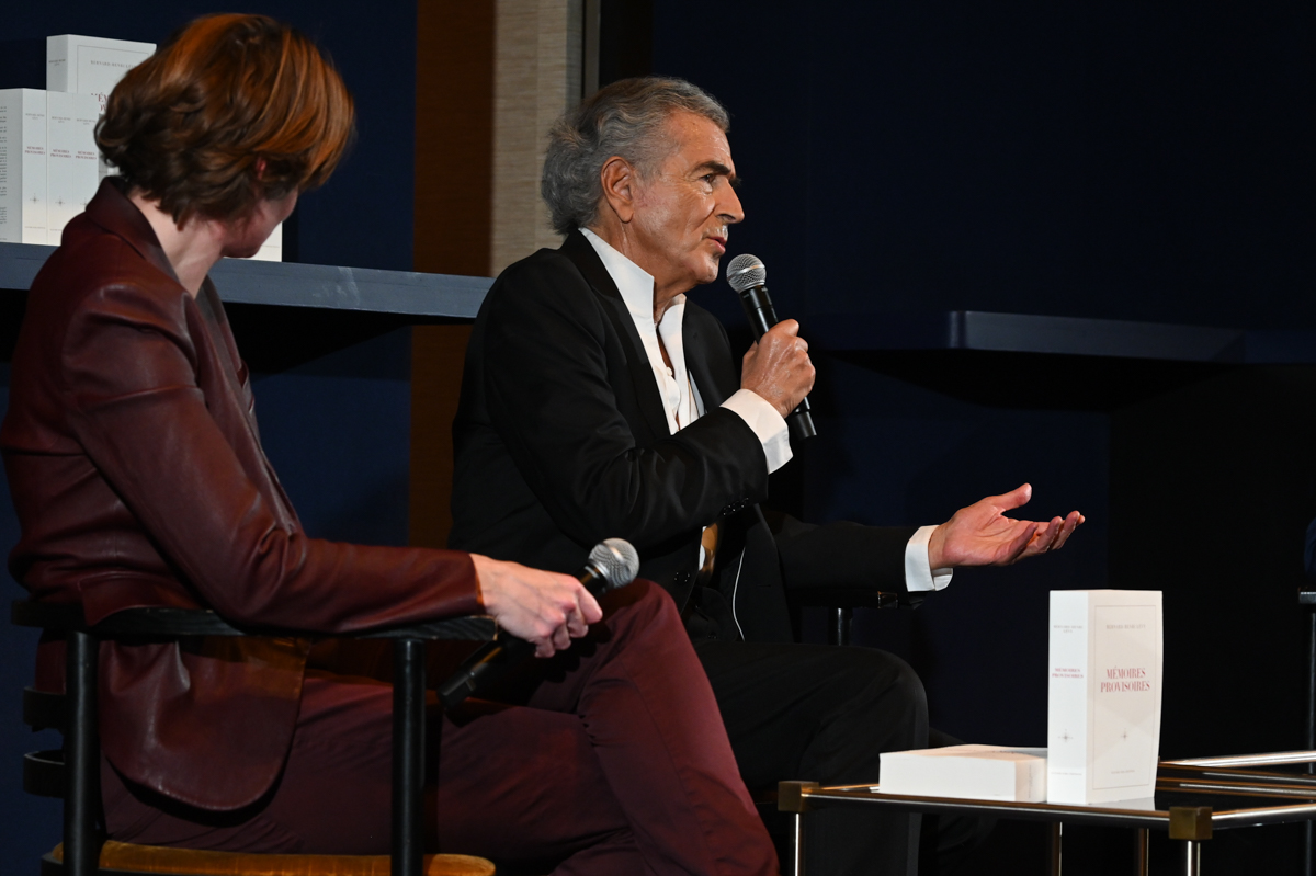 Caroline Fourest assise de dos lors de la soirée de lancement de « Mémoires provisoires » de Bernard-Henri Lévy ; BHL parle dans un micro.